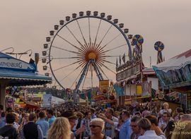 Riesenrad auf dem Oktoberfest in München mit vielen Menschen im Vordergrund bei bewölktem Himmel.